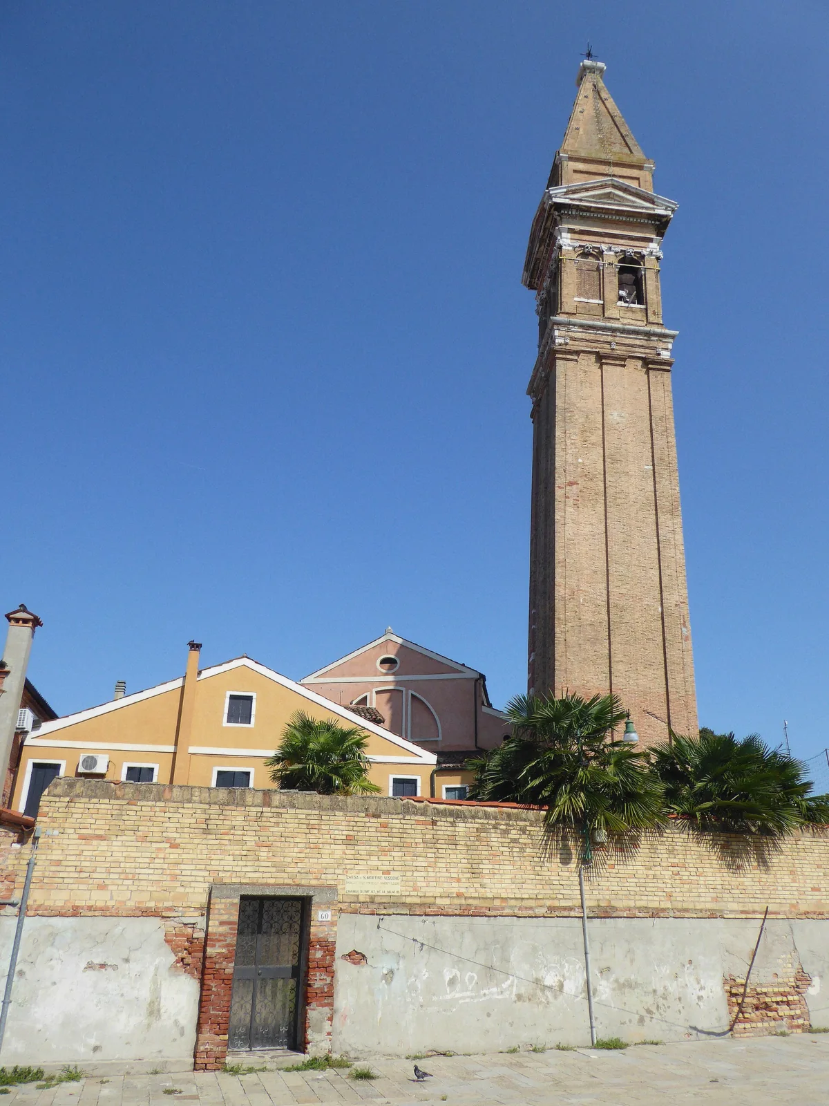 The leaning brick bell tower of Burano above the painted houses, the island's signature sight