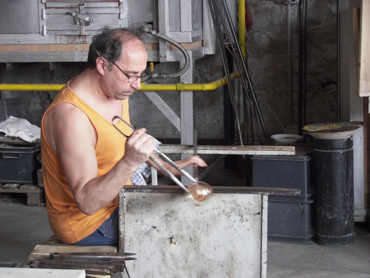 Glass master shaping glowing molten glass at a Murano furnace during the factory demonstration on the boat tour from Venice
