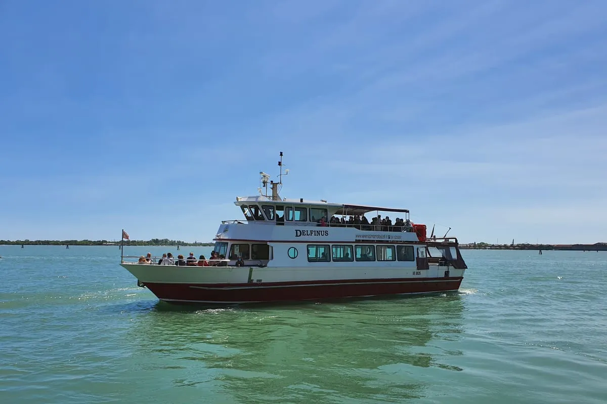 Panoramic boat on the green lagoon water off Burano's painted seafront during a budget Murano and Burano boat tour from Venice, Italy